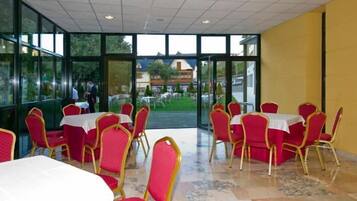 A dining area with tables and chairs, large windows, and a view of the outside.