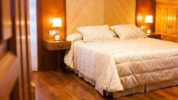 Un dormitorio con techo de madera, una cama con cubrecama blanco, dos mesitas de noche con lámparas y piso de madera.