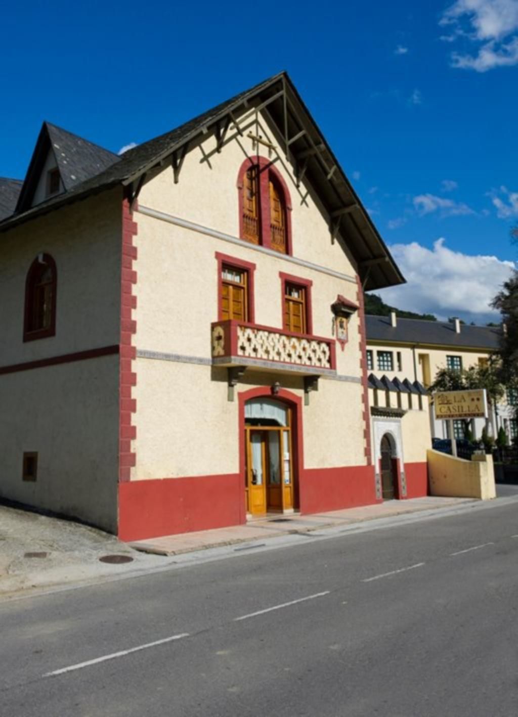Un edificio con fachada roja y blanca, un balcón con barandilla decorativa y un letrero que dice "LA CASILLA".