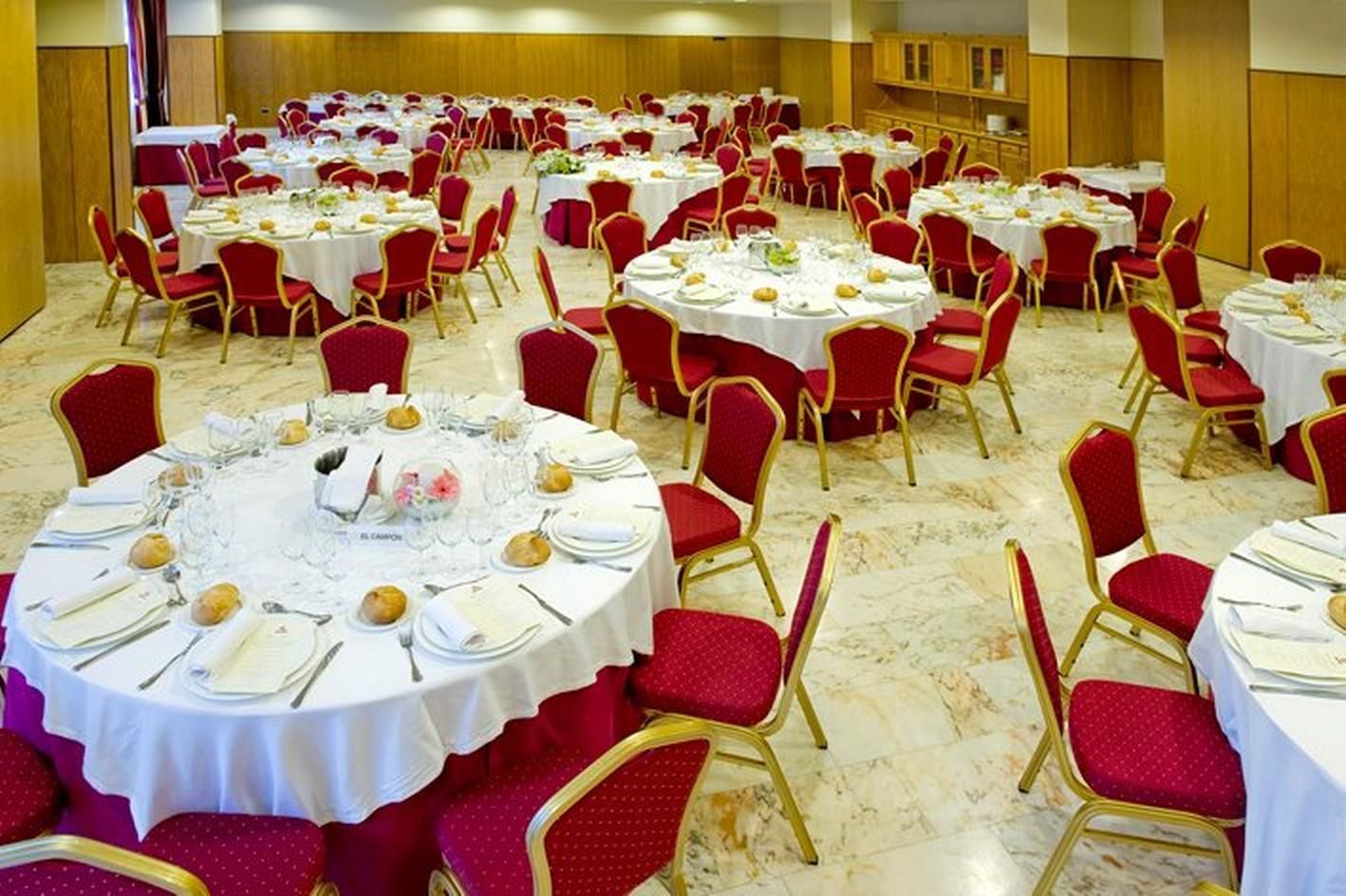 Una sala de banquets amb taules rodones preparades per a dinar, cadires tapissades de color vermell i un paviment de marbre.