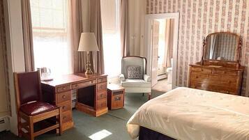 Une chambre d’hôtel avec un lit, un bureau et une chaise, une commode et une chaise avec un coussin.