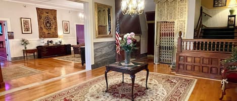 A spacious lobby with a wooden floor, a chandelier, a reception desk, and a staircase.