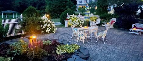 An outdoor patio area with a stone-tiled floor, white wicker furniture, and a white picket fence.