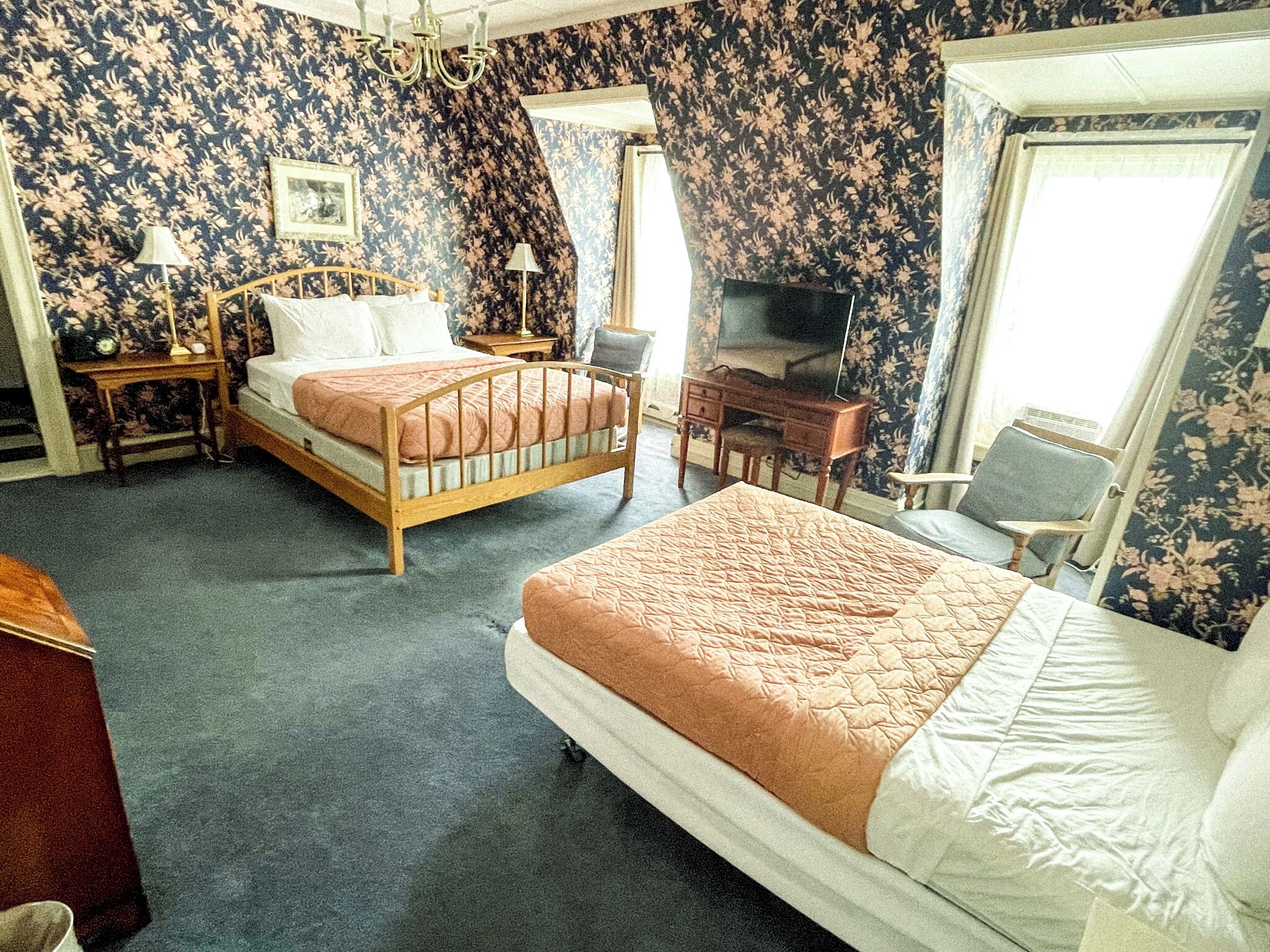 A hotel room with two beds, a desk, a television, and a chair.