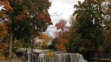 A waterfall surrounded by trees with autumn foliage, a stone bridge, and a house in the background.