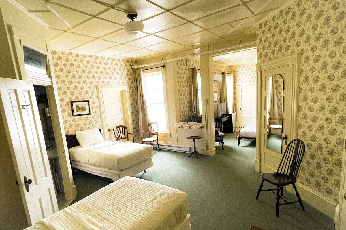 A hotel room with two beds, a desk, a chair, a television, and a mirror.