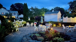 Un patio empedrado con mobiliario exterior, un parterre decorativo y una valla blanca.