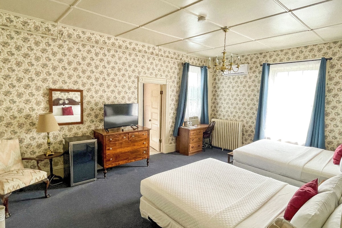 A hotel room with two beds, a TV, a dresser, a chair, and a desk.