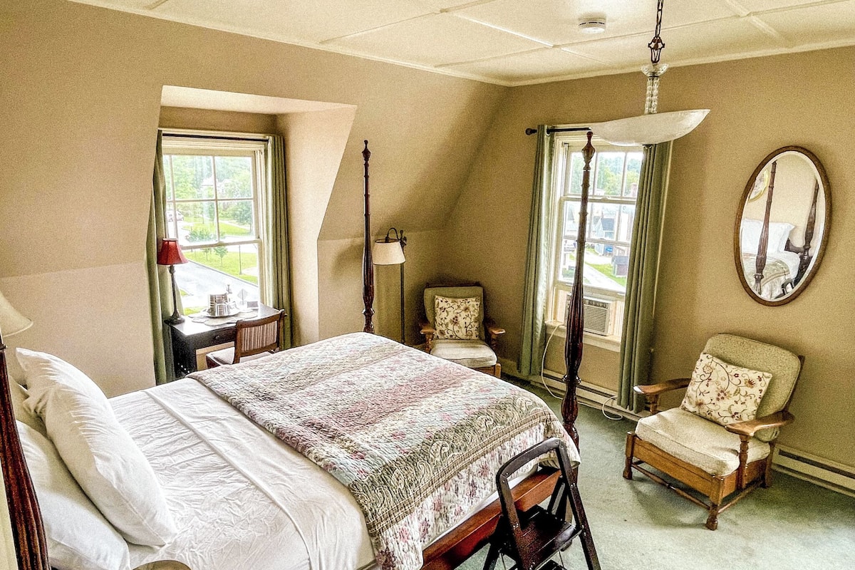 A bedroom with a bed, a chair, a desk, and a window.