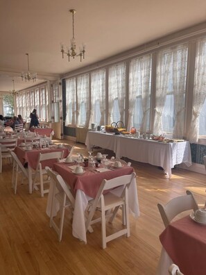 A dining area with tables set for a meal, large windows with curtains, and chandeliers. - Brandon Inn (Brandon)