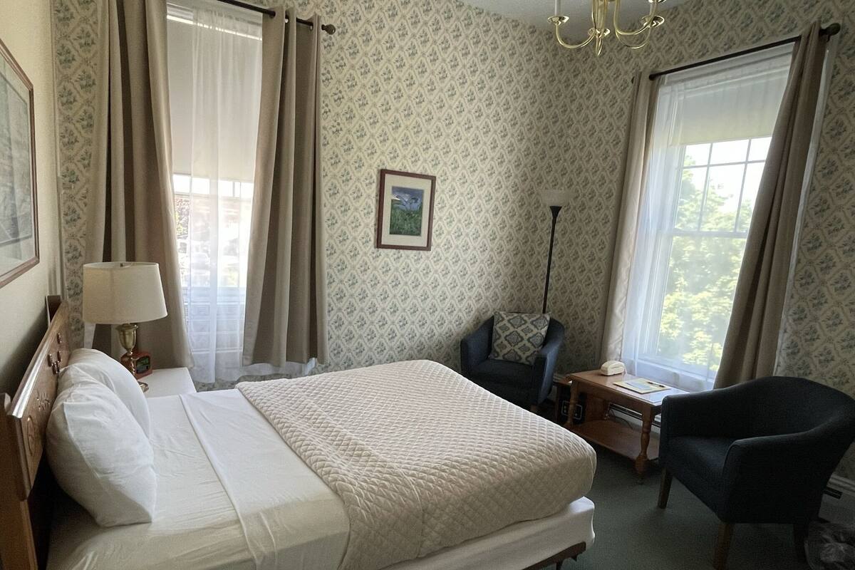 A hotel room with a bed, a desk, a chair, a lamp, and a picture on the wall.