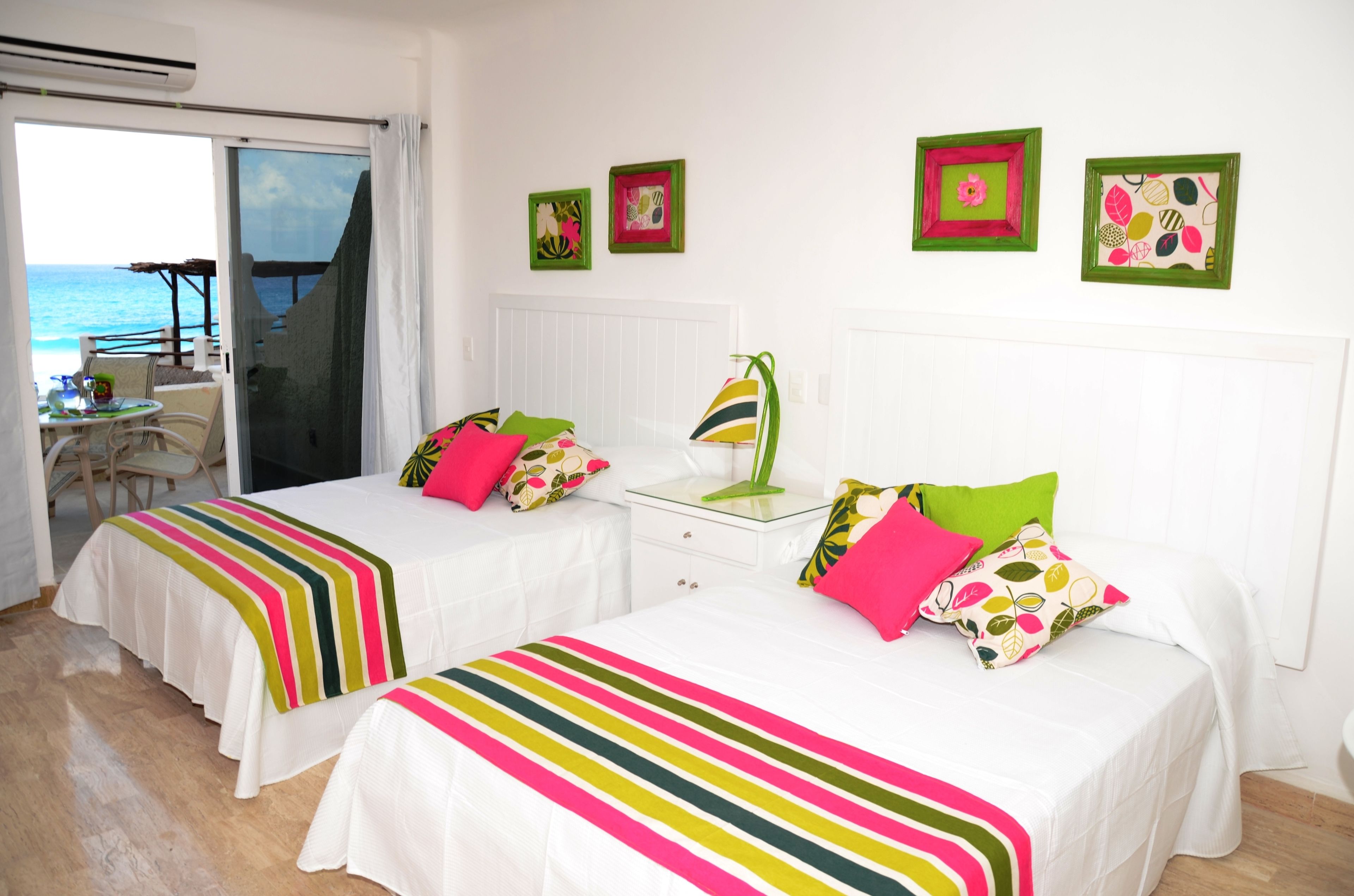 A hotel room with two beds, a balcony with a view of the sea, and artwork on the walls.