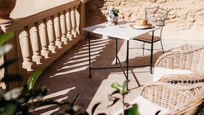 An outdoor patio with a stone wall, a table with chairs, and wicker furniture. - Hotel Casa Peya - Adults Only (Palafrugell)