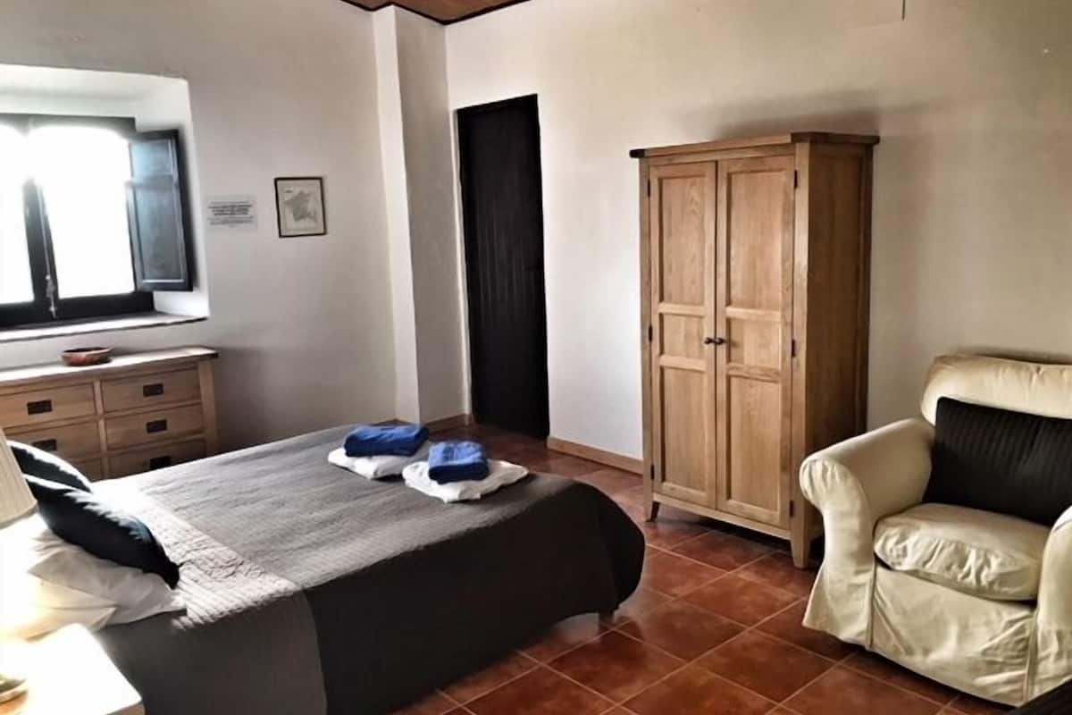 Une chambre à coucher avec un lit, une armoire en bois, une chaise et un bureau avec une lampe.
