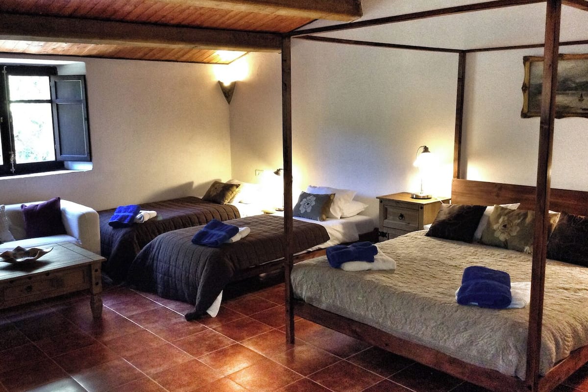 Un lit à baldaquin avec un cadre en bois, deux tables de chevet avec des lampes, une fenêtre avec des volets et un sol carrelé.