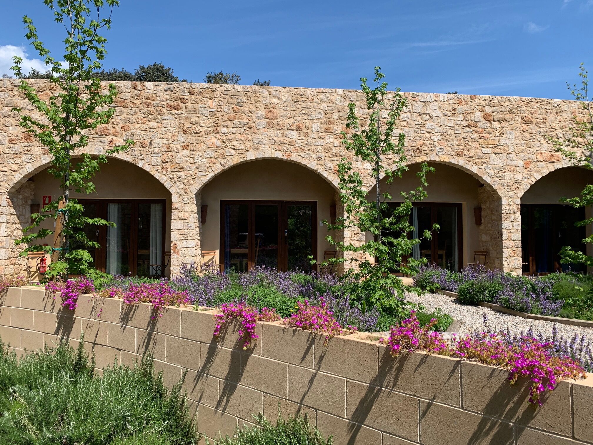 A stone building with three arched windows and a garden with purple flowers.