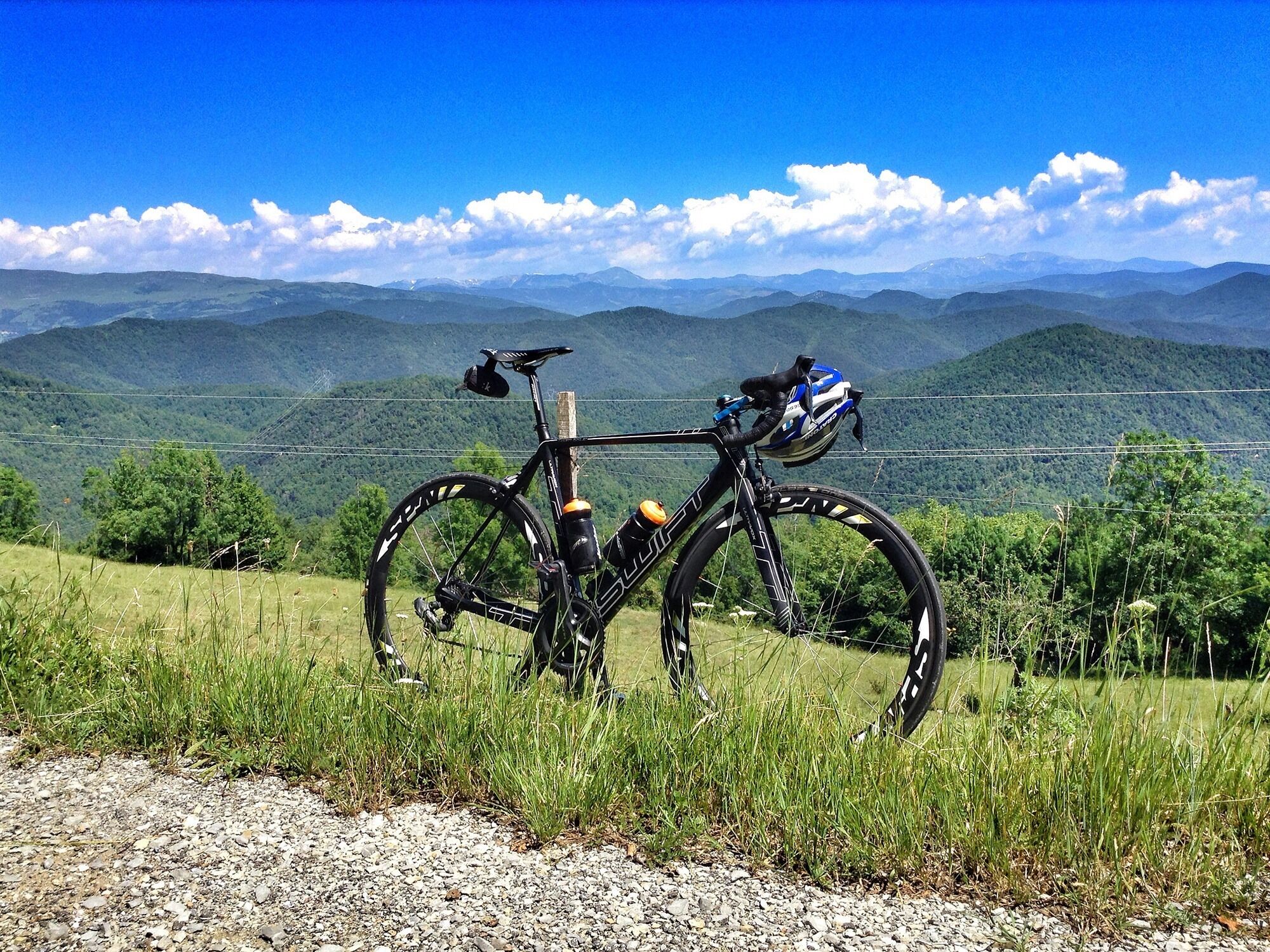 Una bicicleta estacionada en un camino de grava con una vista panorámica de montañas y vegetación al fondo.