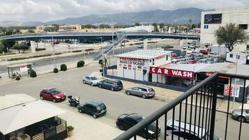 Un centre de lavage automobile avec plusieurs voitures stationnées sur le parking, un pont piétonnier et un paysage montagneux en arrière-plan.