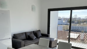 Un espacio habitable moderno con un sofá gris, una mesa de comedor con sillas y un amplio ventanal corredero que da a un balcón.