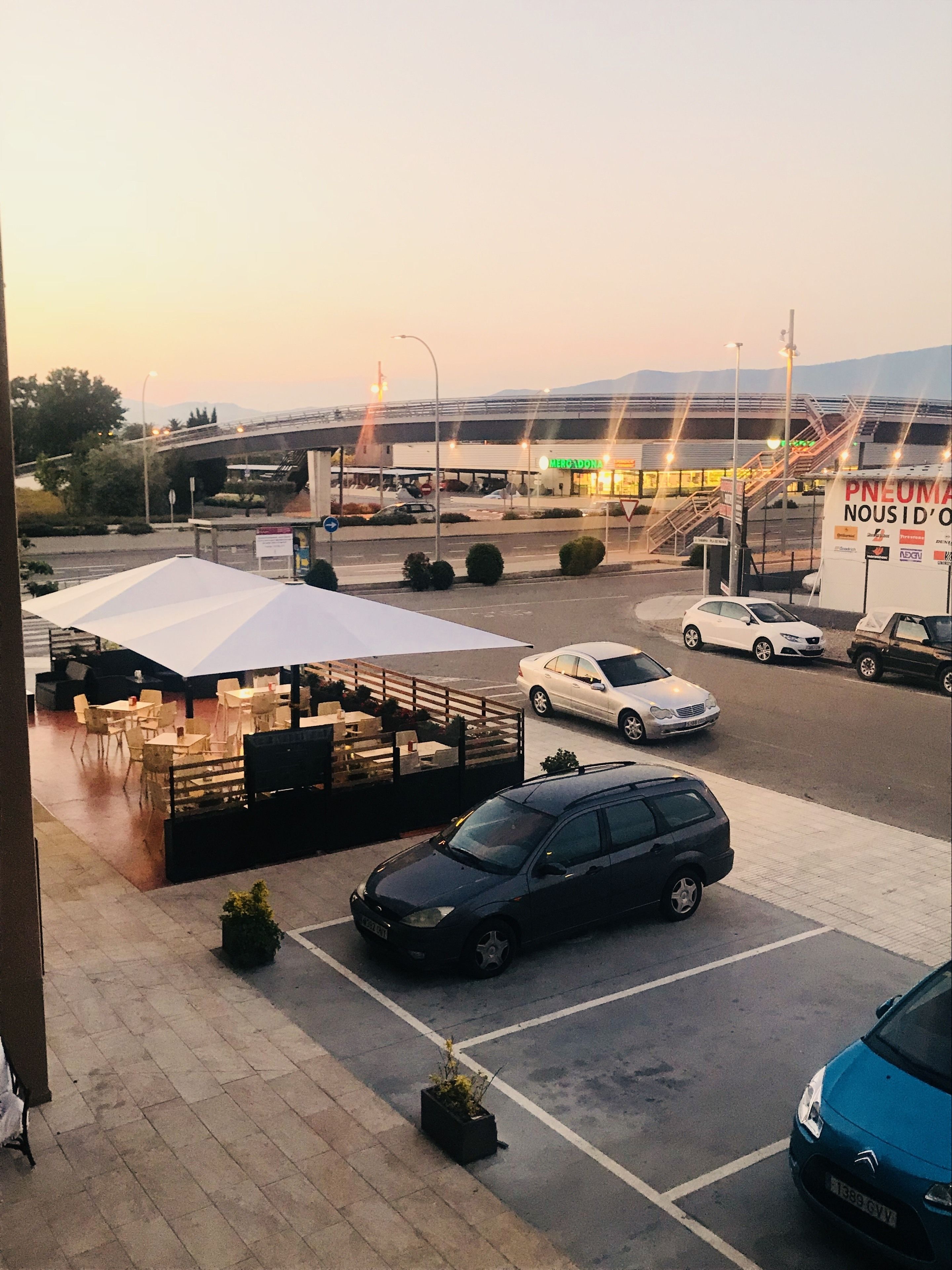 A parking area with a white tent, a black car, and a blue car.