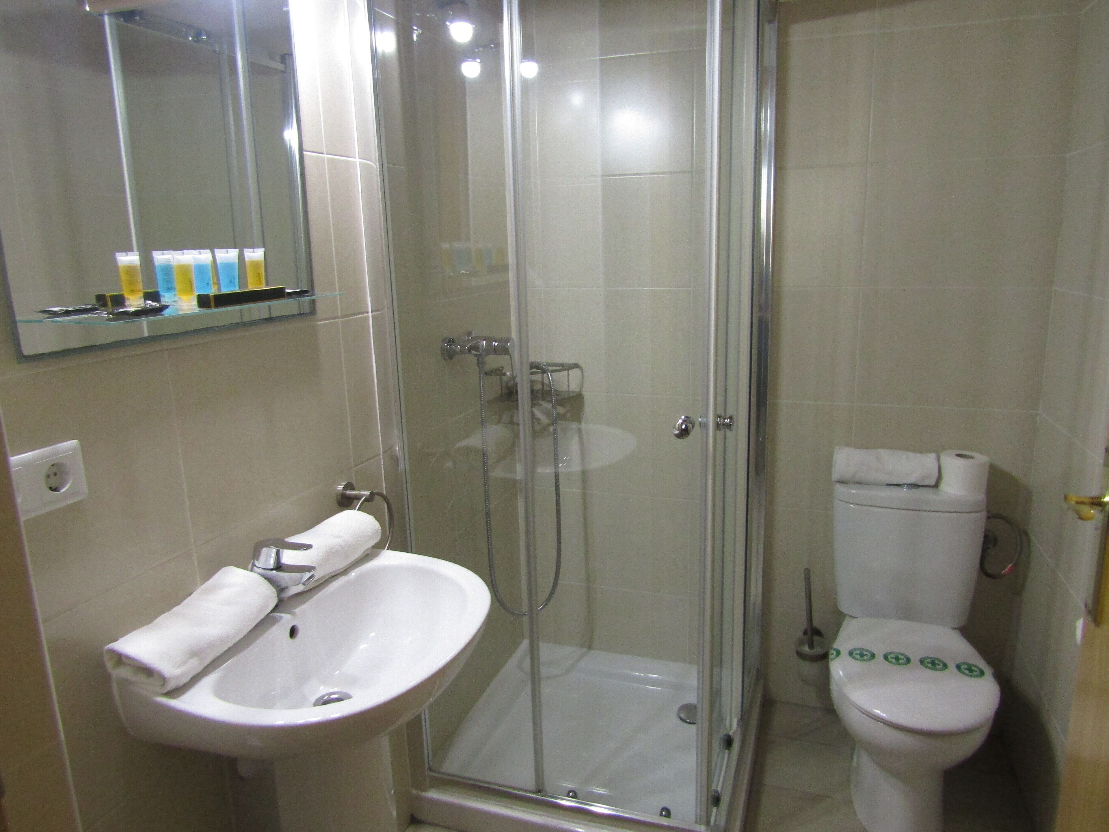 Un baño con ducha envuelta en vidrio, lavamanos y retrete.
