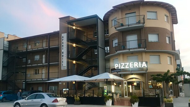 Un edificio de varios pisos con un letrero que dice 'PIZZERIA', un letrero que dice 'GUILIANO PART HOTEL' y un estacionamiento con coches.