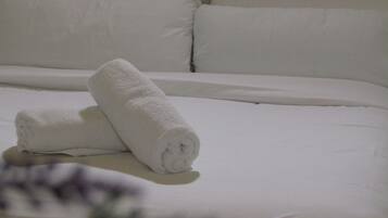 Un lit bien fait, avec du linge de lit blanc et une serviette blanche enroulée posée sur le dessus.