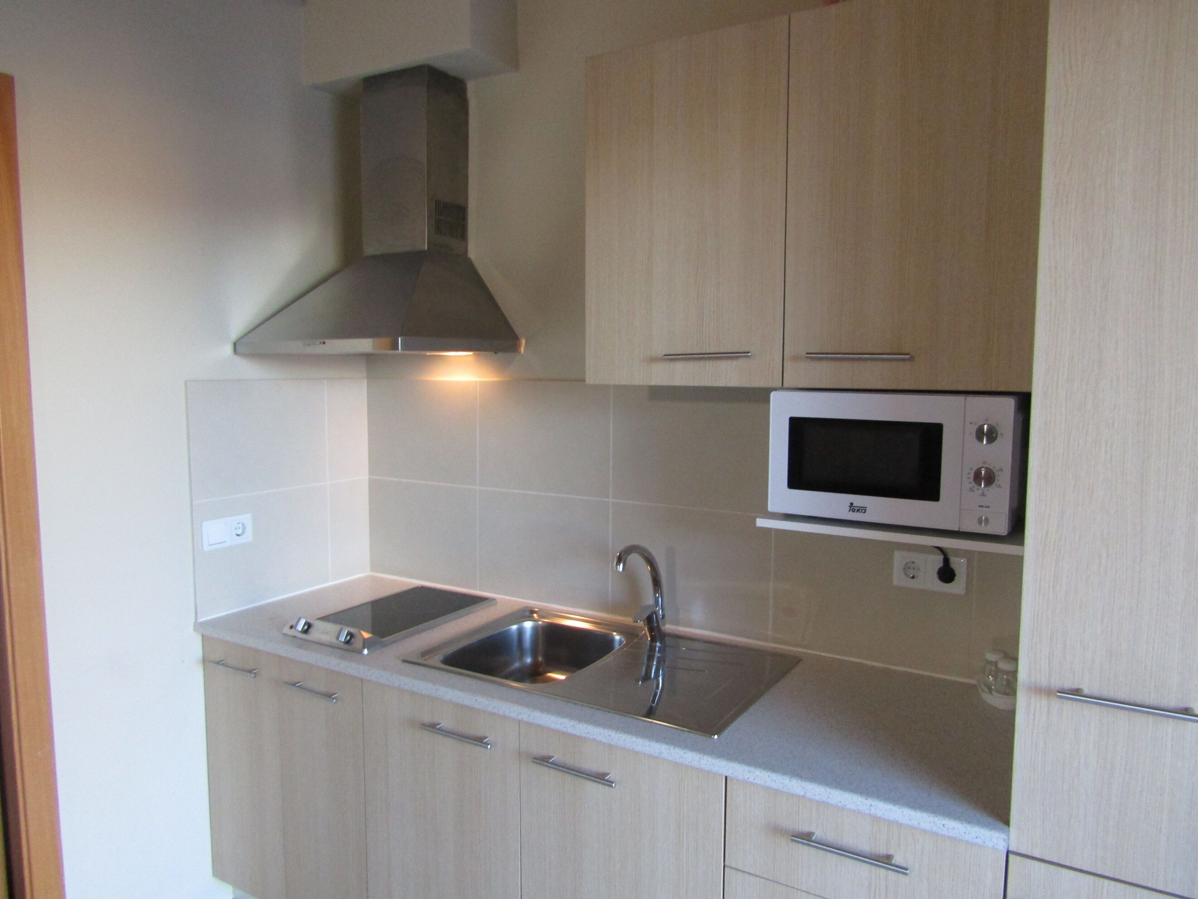 A kitchen with light wood cabinets, a stainless steel sink, a double oven, and a microwave.