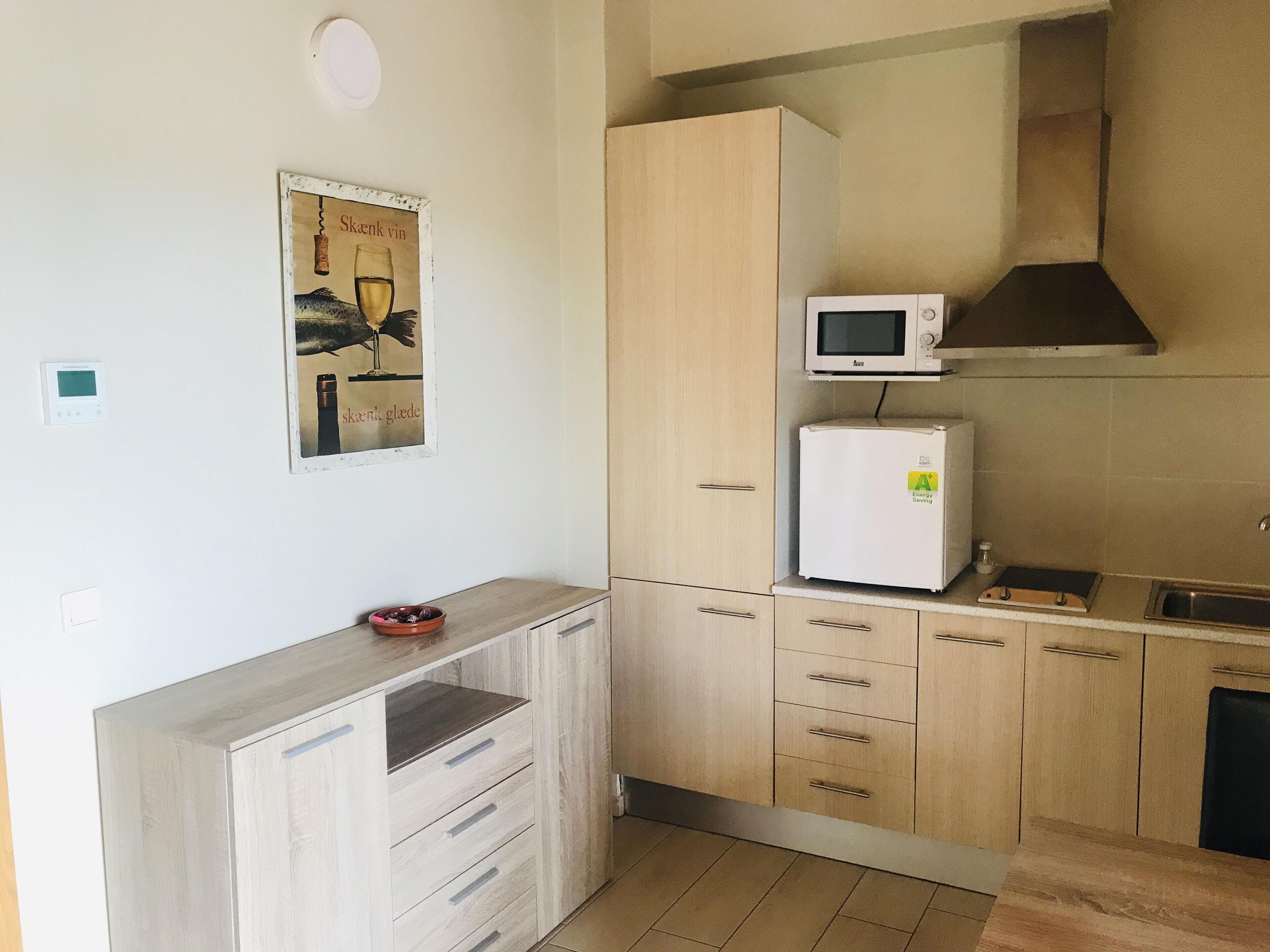 A compact kitchen with a microwave, a small refrigerator, and a wooden cabinet.