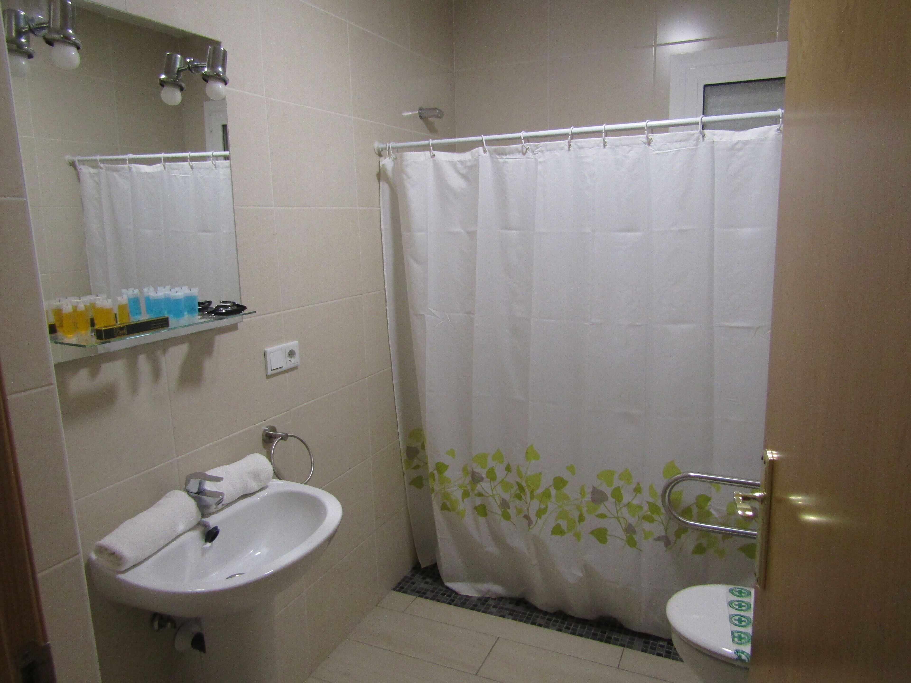 Un baño con lavamanos, espejo, cortina de ducha y estante con artículos de aseo.