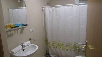 Un baño con lavamanos, espejo, cortina de ducha y estante con artículos de aseo.