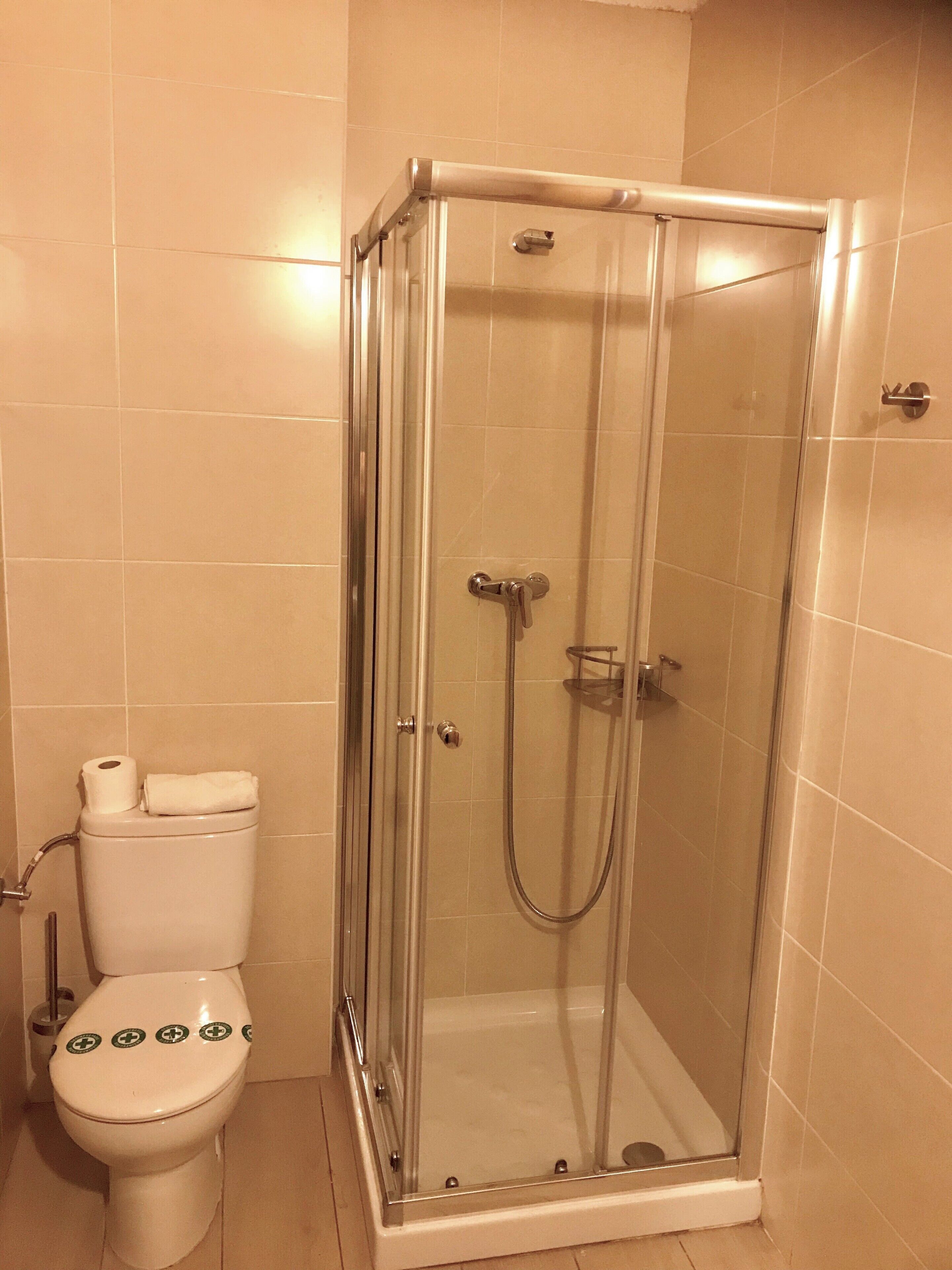 Un baño con ducha de vidrio, un inodoro y un rollo de papel higiénico sobre el tanque.