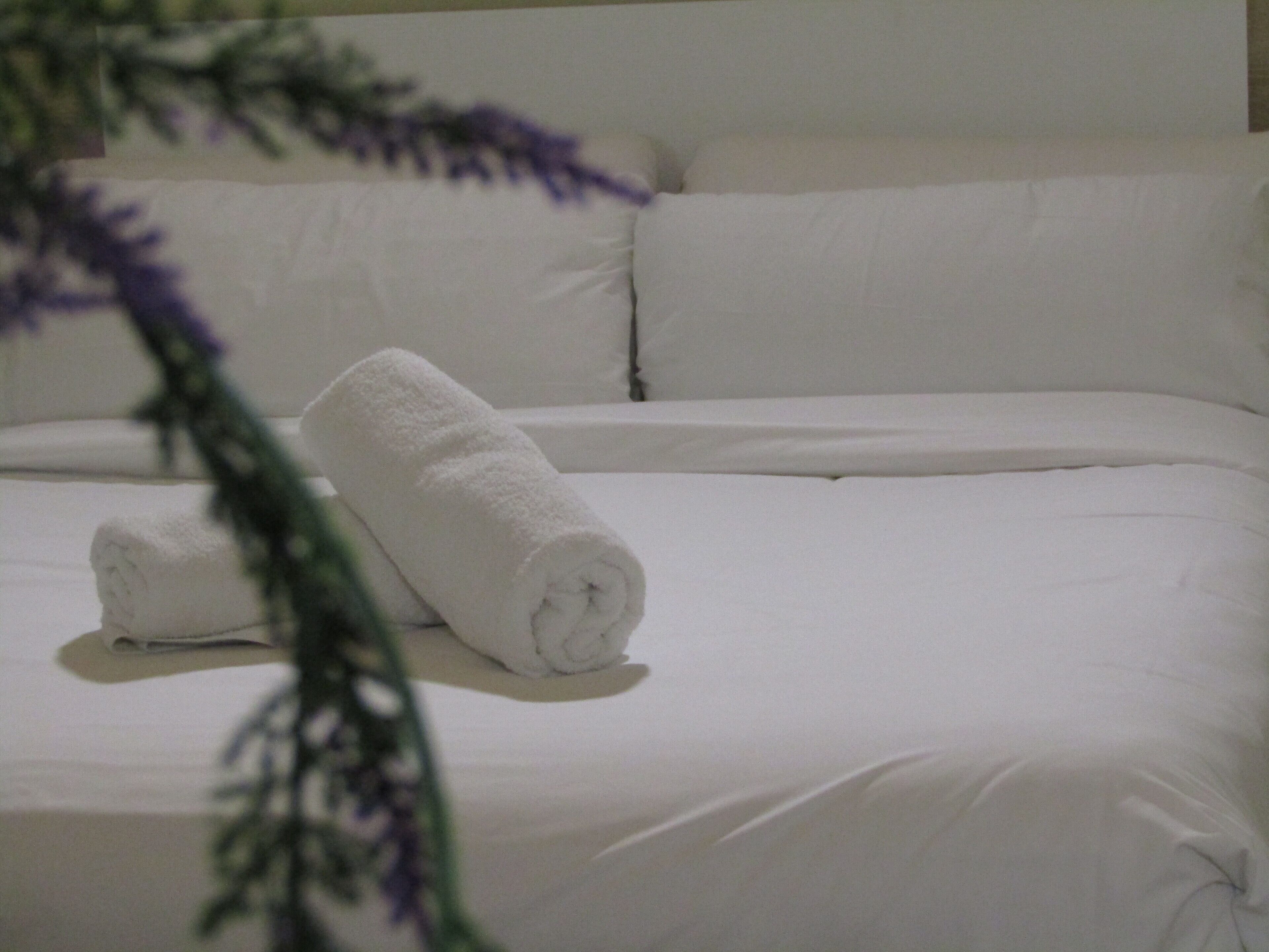 A neatly made bed with white linens and a rolled towel on the side.