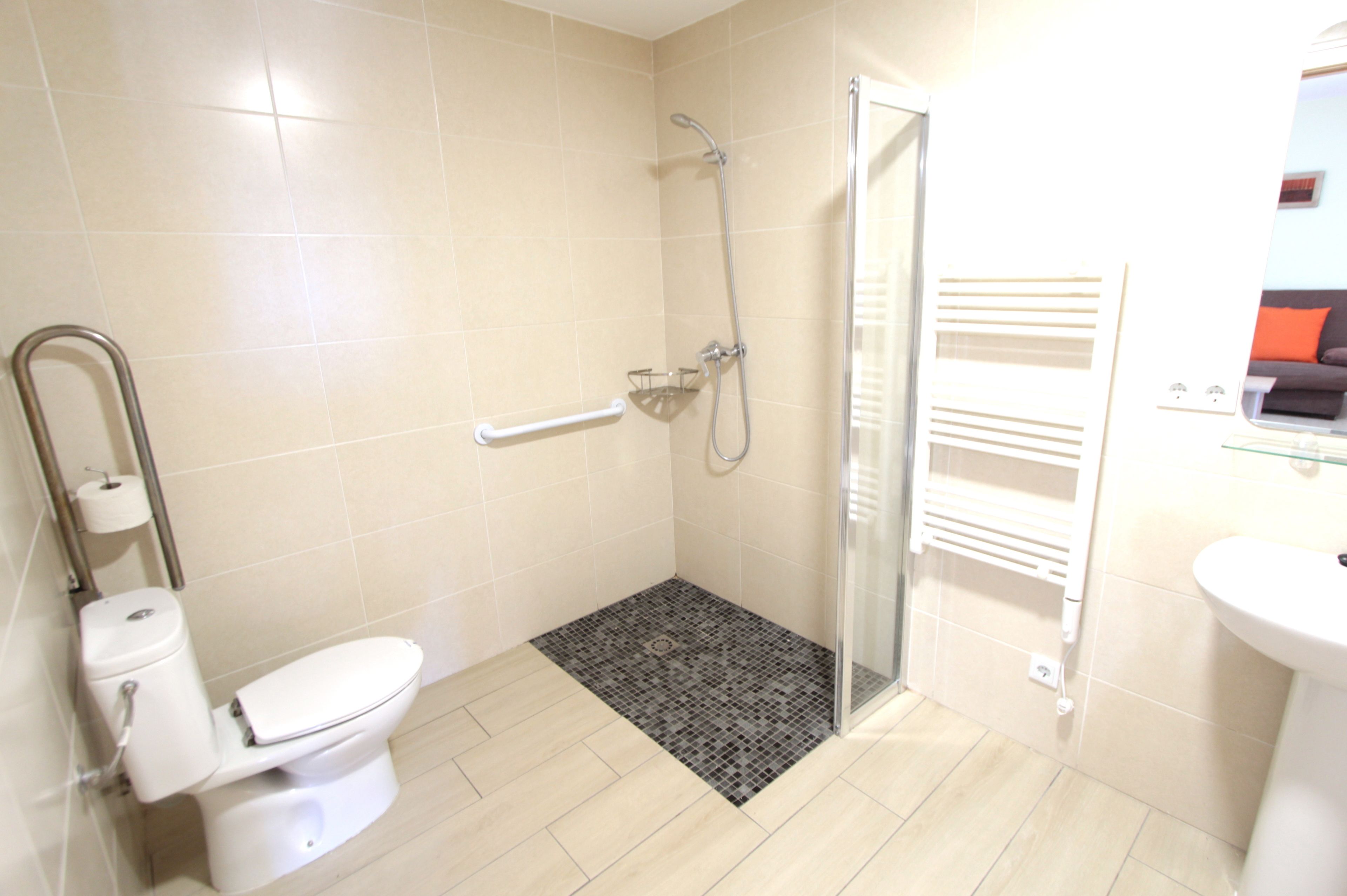 A bathroom with a toilet, a shower with a glass door, a small rug, and a sink.