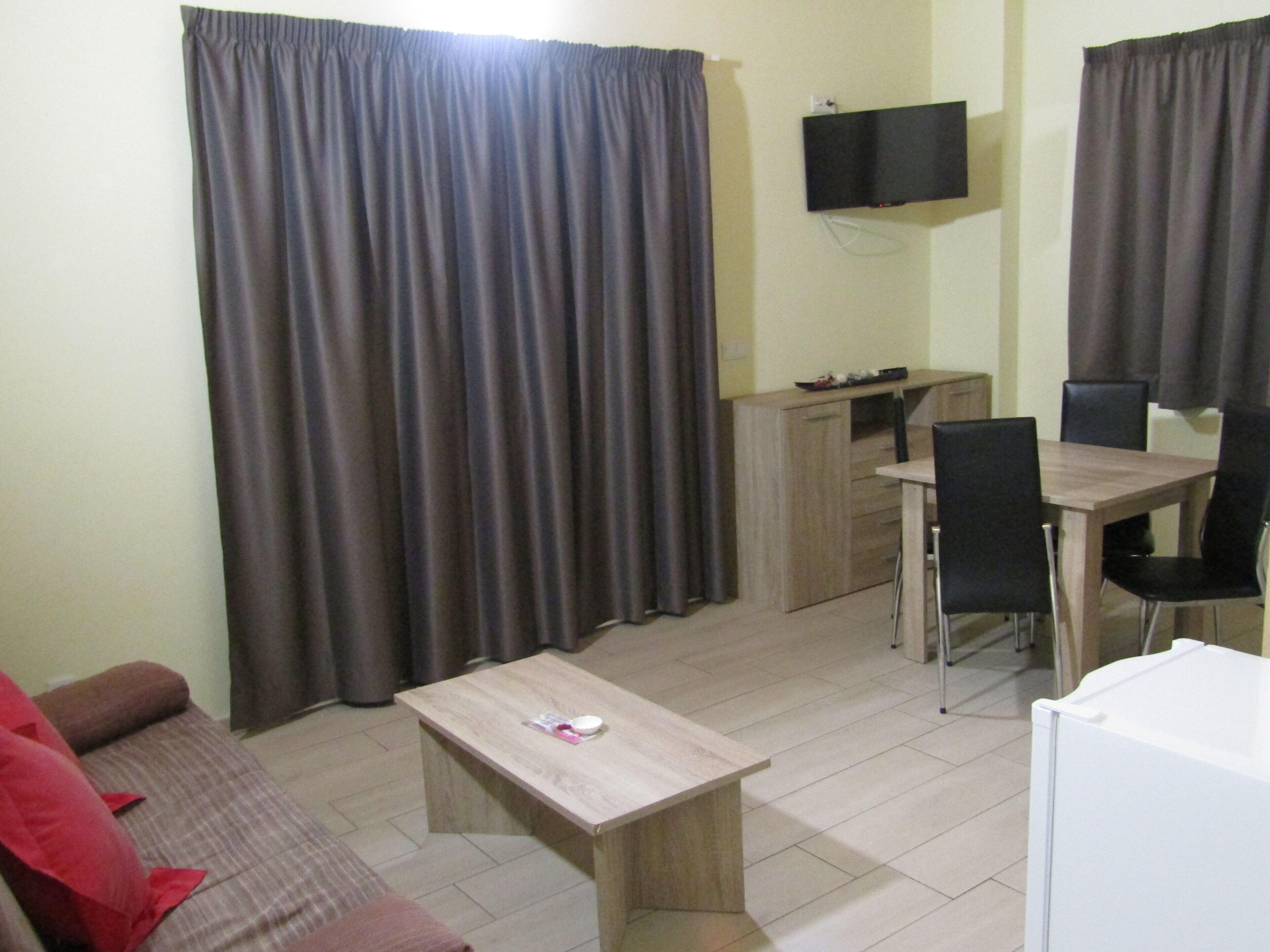 Una habitación pequeña y amoblada con un sofá, una mesa, un escritorio y un televisor montado en la pared.