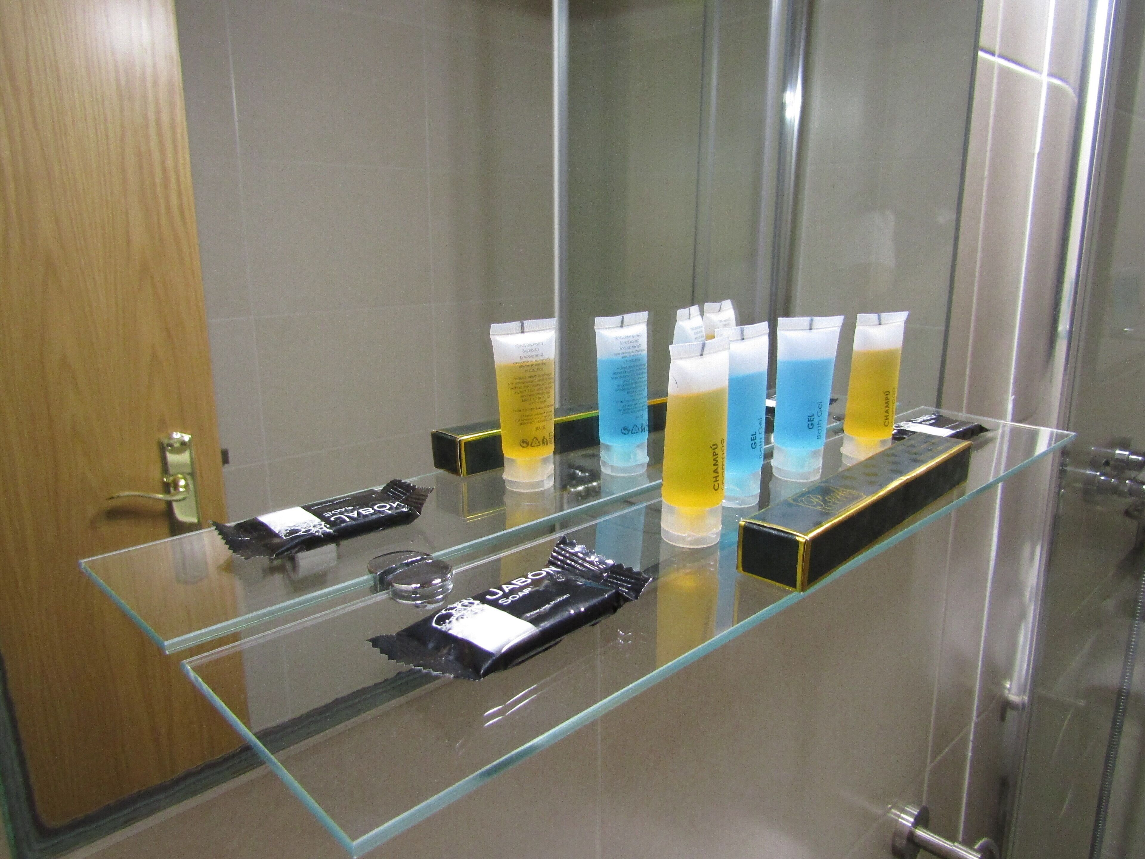 Ein Badezimmer mit einer Glasablage, auf der verschiedene Pflegeprodukte stehen, und einem Duschbereich.