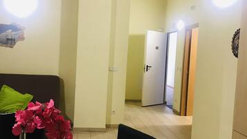 A room with a wooden ceiling, a sofa with green cushions, a vase with pink flowers, and a door leading to another room.