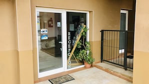 Un área de recepción con puerta de cristal, una planta en maceta y una reja de metal negro.