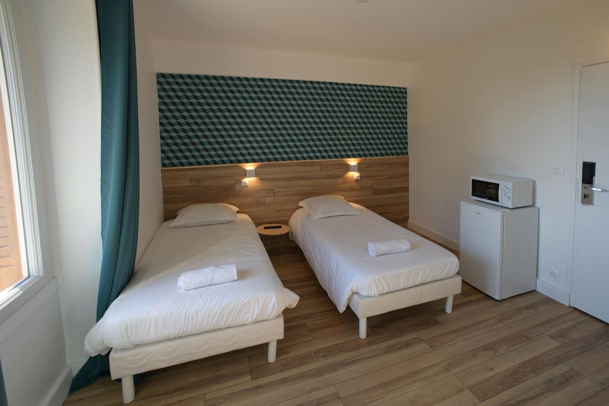 Een kamer met twee eenpersoonsbedden, een houten hoofdbord, een klein wit kastje en een magnetron.