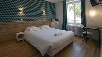A bedroom with a wooden headboard, a bed with white linens, a small bedside table, a wall-mounted TV, and a window with curtains.