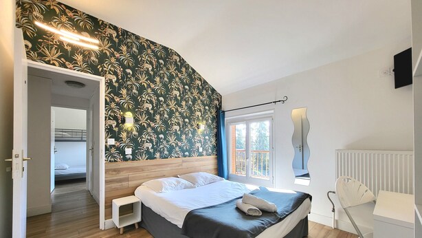 A bedroom with a bed, a nightstand, a mirror, and a window with a view of trees.