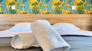 A hotel room with a wooden headboard, a bed with white linens, and a tropical leaf-patterned wallpaper. There are two wall-mounted lights on either side of the bed.