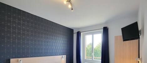 A modern hotel room with a large bed, bedside tables, a desk, and a TV.