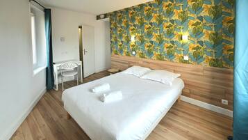 Un dormitorio con cabecera de madera, cama con sábanas blancas, un escritorio con silla y una pared con estampado de hojas.