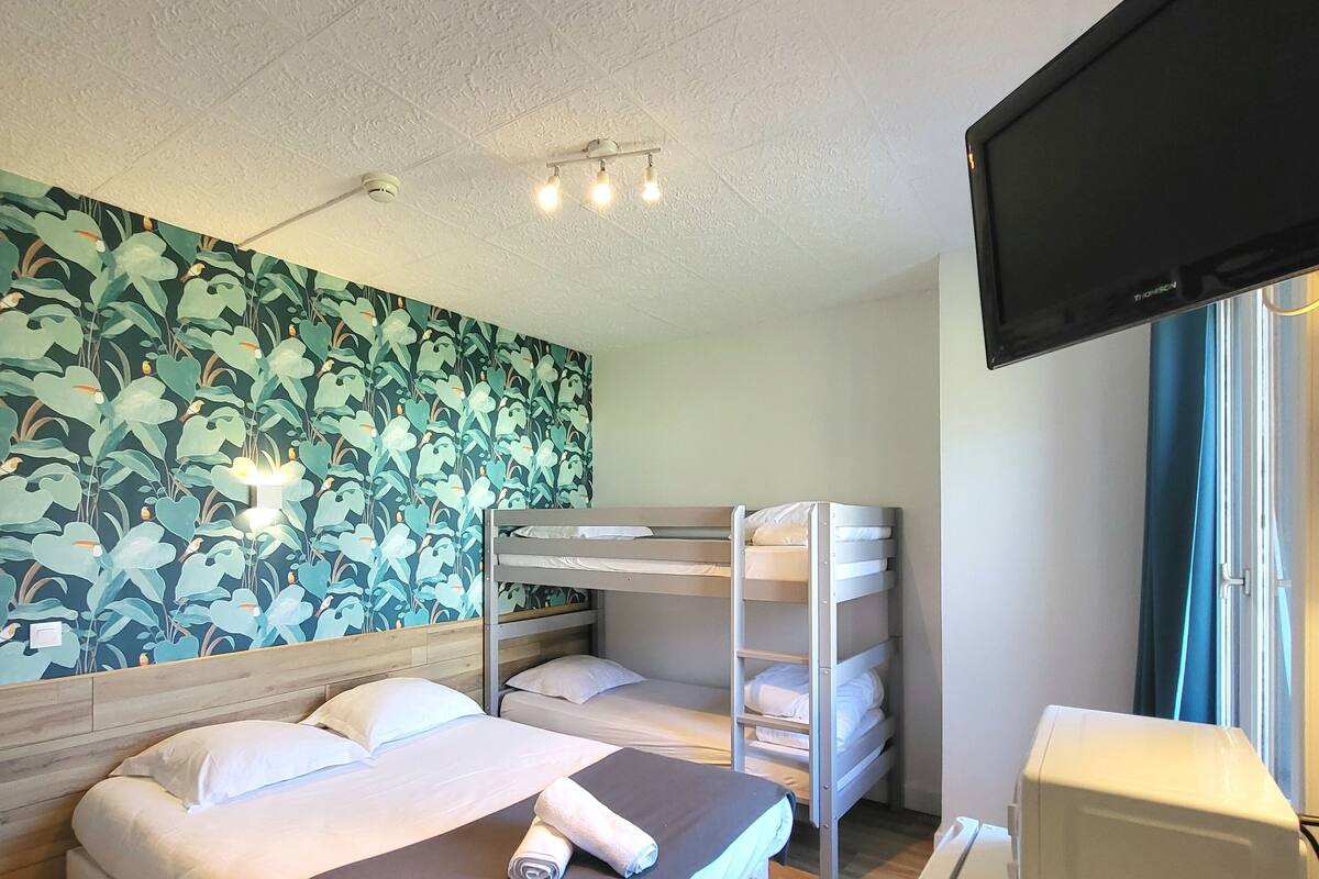 Een hotelkamer met een stapelbed, een bureau met een computer, een televisie en een muur met een bladpatroon.