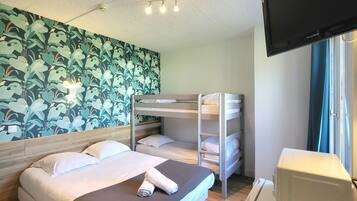 A hotel room with a bunk bed, a desk with a computer, a TV, and a wall with a leafy pattern.