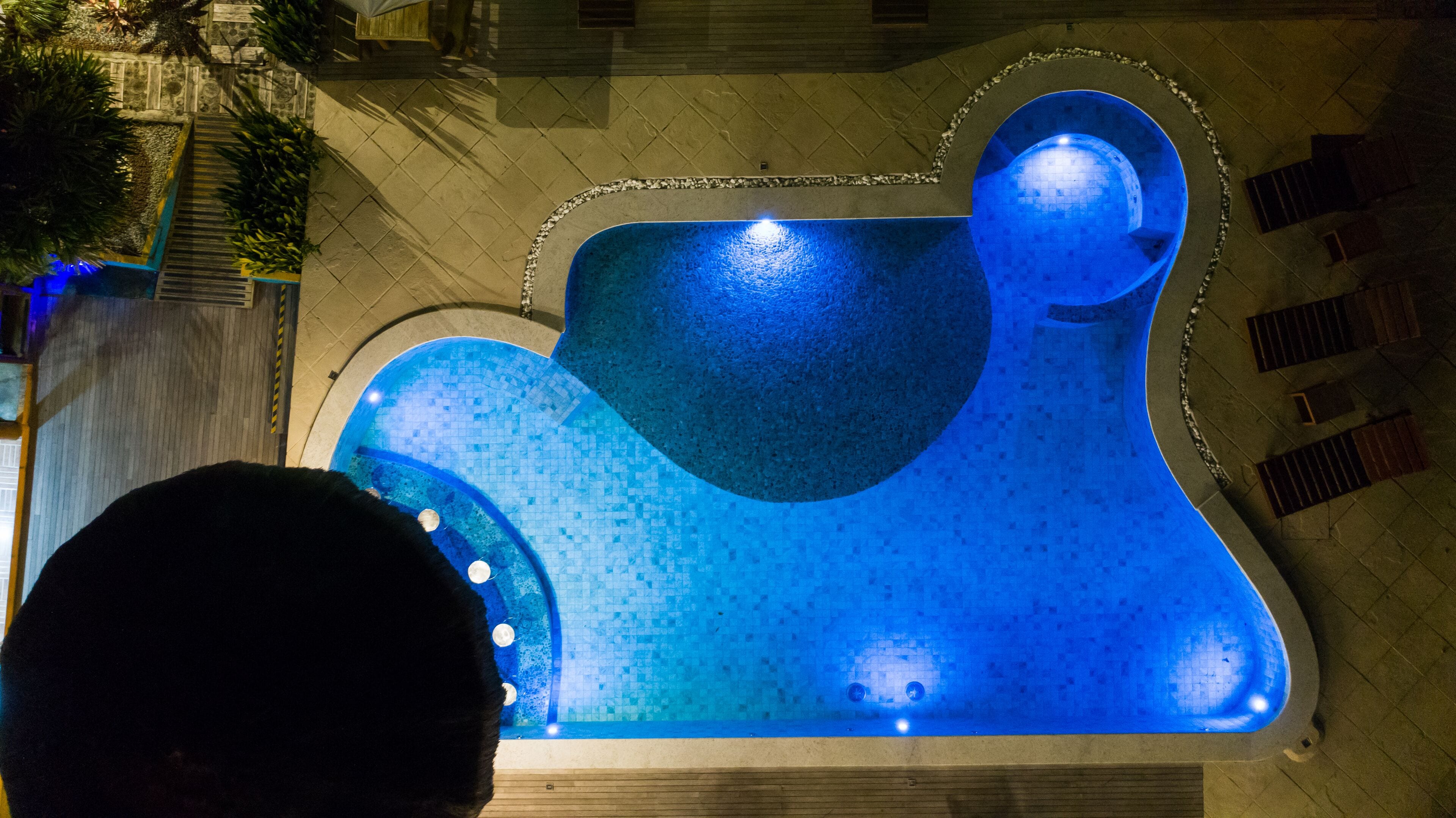 A swimming pool with a unique design, surrounded by a tiled deck and a stone wall.