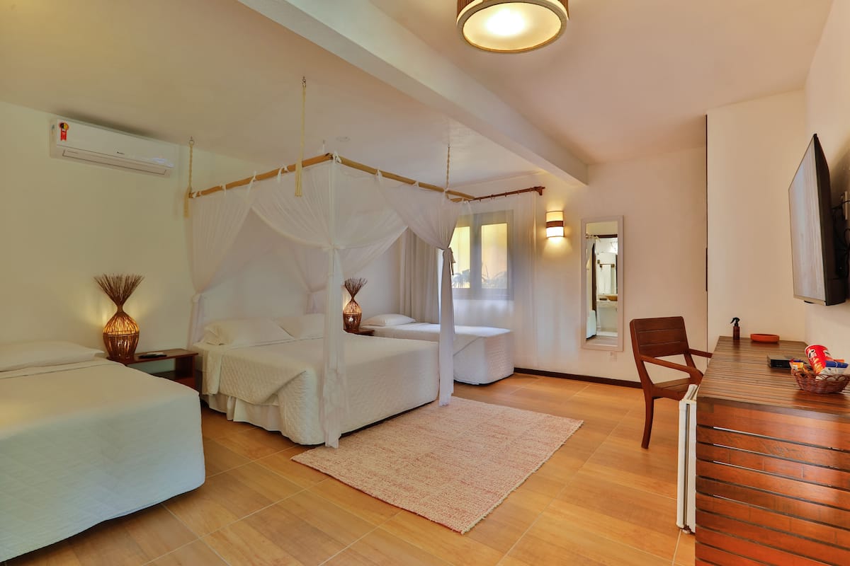A bedroom with a canopy bed, a sitting area with a chair, a dining table, and a TV mounted on the wall.