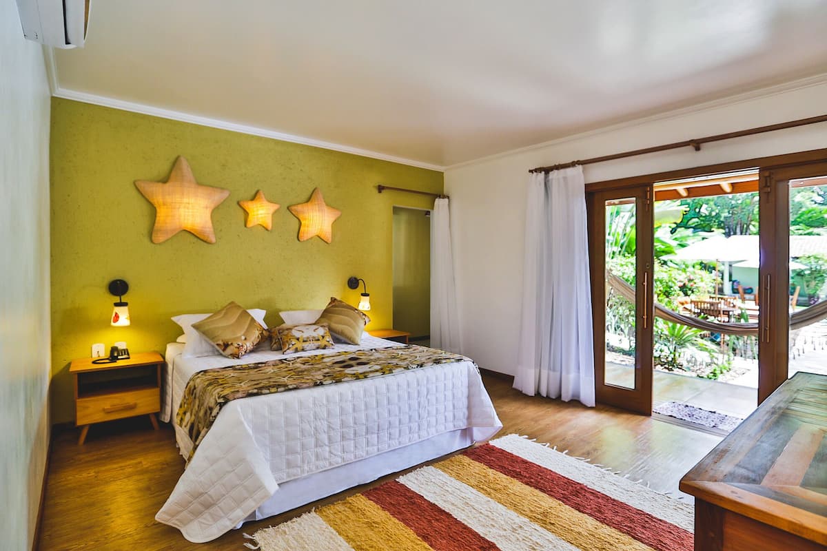 A bedroom with a bed, bedside lamps, a star wall decoration, and a view of a garden through a sliding door.
