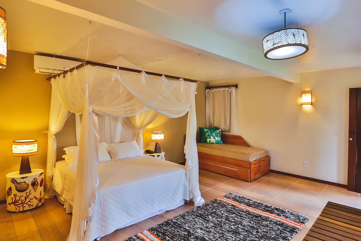 A bedroom with a four-poster bed, bedside lamps, a nightstand, a bench, and a wall-mounted light fixture.